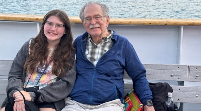 Grandparent and grandchild on a seat on a boat, smiling at the camera.