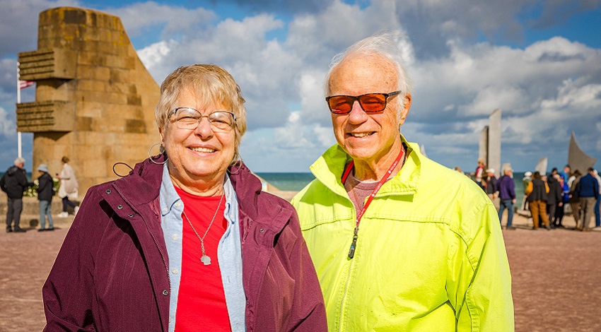 Two Road Scholars at Omaha Beach, with monuments in the background