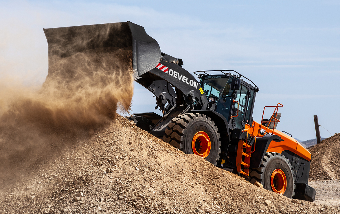 A DEVELON wheel loader bucket dropping dirt uphill.