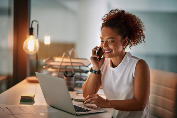 woman smiling at laptop holding phone woman smiling at laptop holding phone