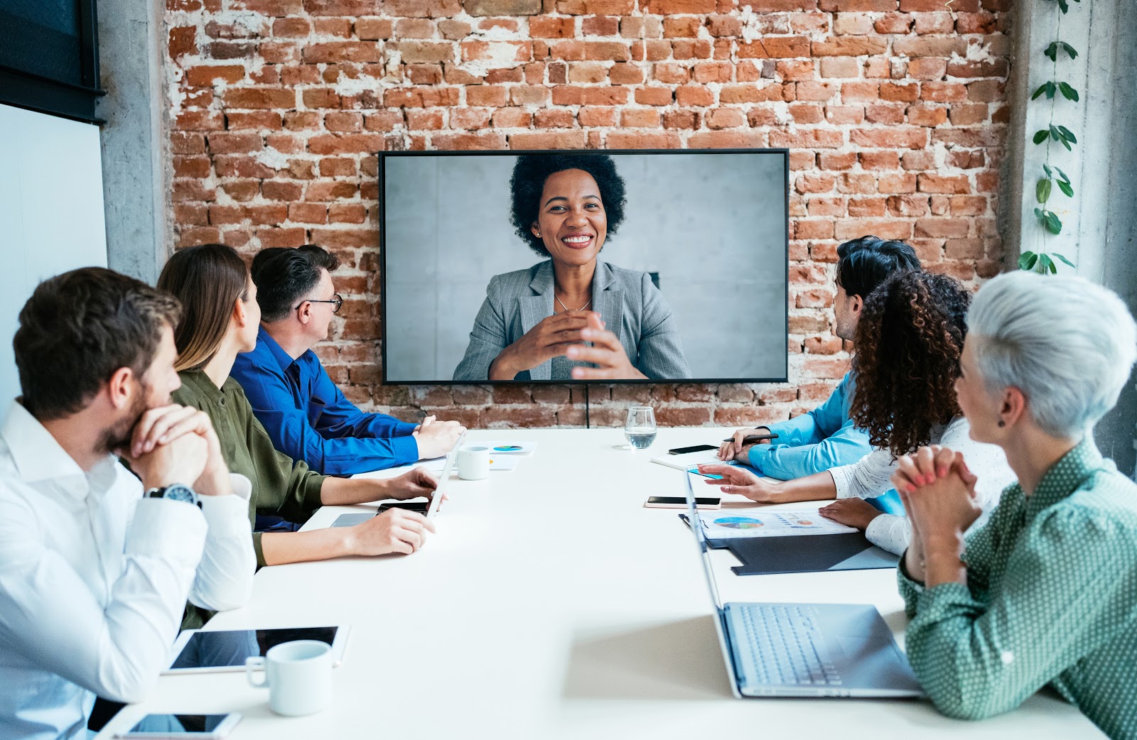 Business people meeting around conference table and looking at woman on screen in video conference